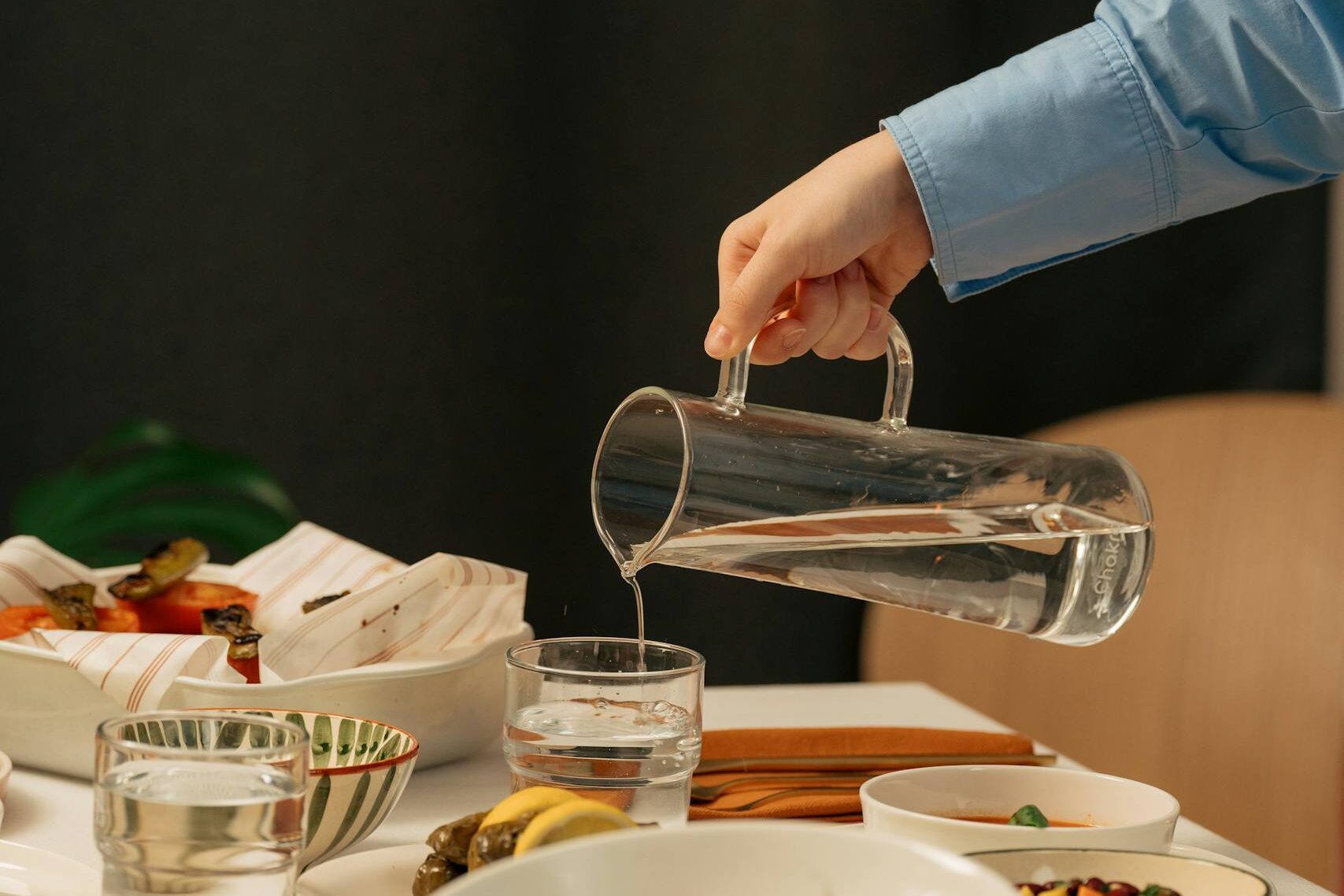 A person pours water at a beautifully arranged dinner table during a festive meal.